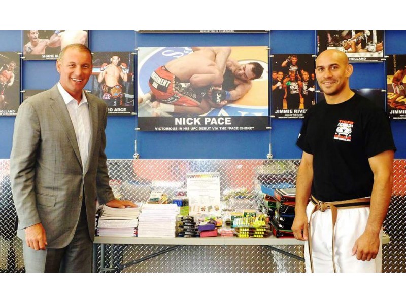 A man in a suit and a MMA fighter posing in front of donated supplies