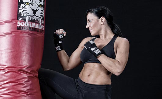A woman kickboxer kicking a punching bag