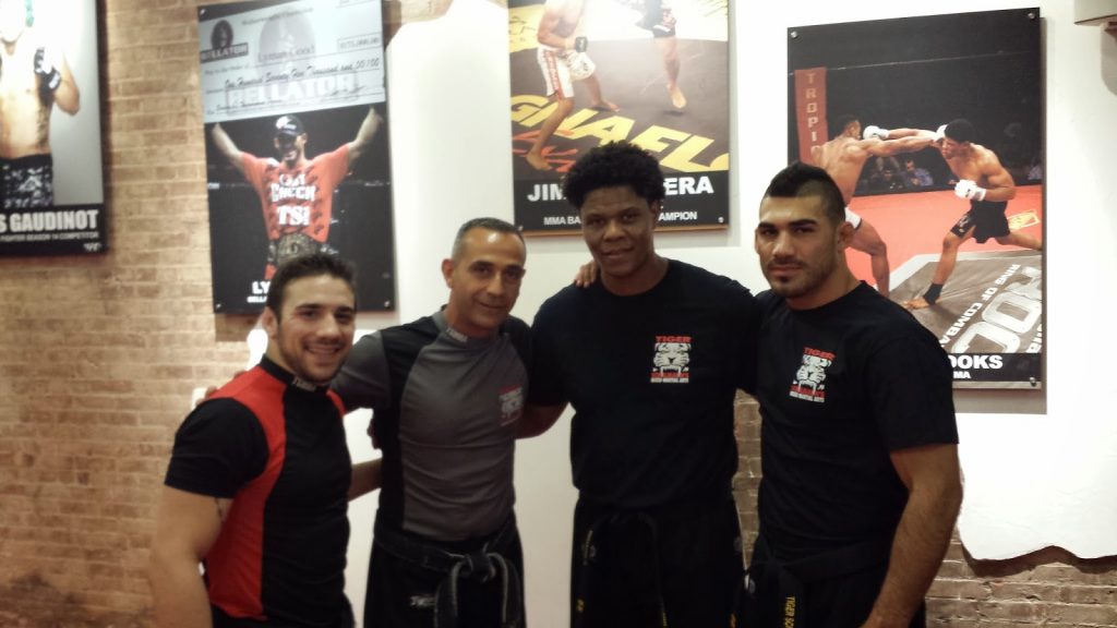 Four MMA fighters with a wall with photos at Tiger Schulmann's