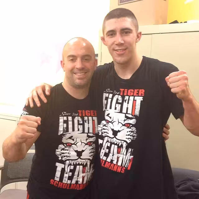 Two Men Wearing TSMA Shirts in a room