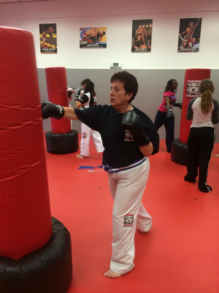 Woman Punching a red bag with other adults working out in the back at Tiger Schulmann's