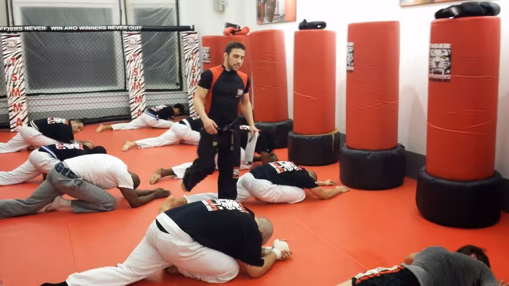 Men fighters streching on the floor with instructor walking at Tiger Schulmann's