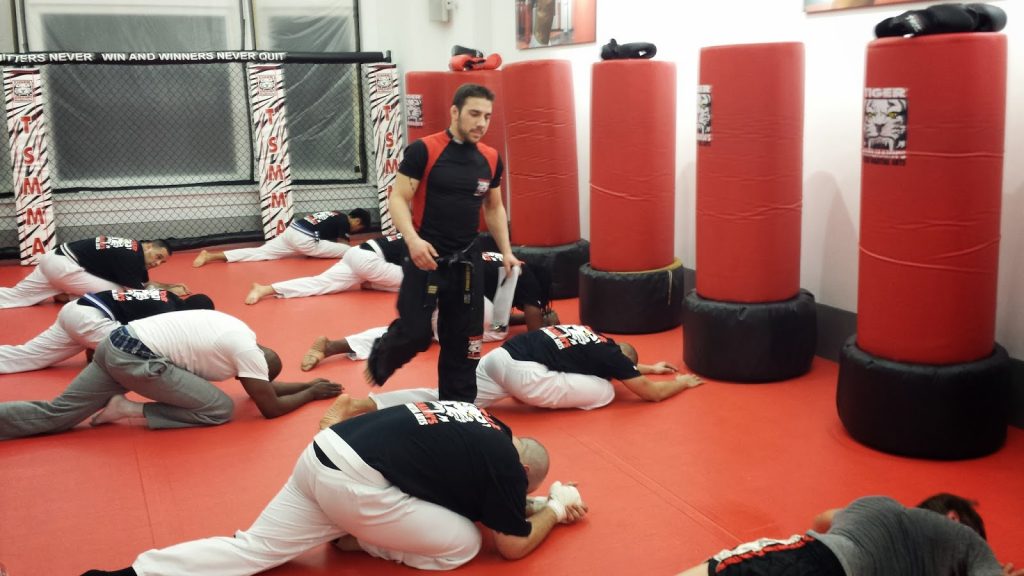 Men fighters streching on the floor with instructor walking at Tiger Schulmann's