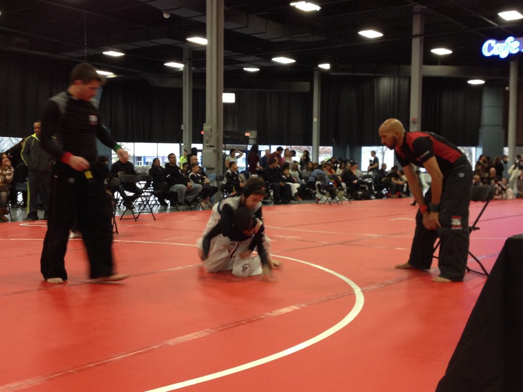 Two boys Grappling on the gym floor during the tournament with referee standing