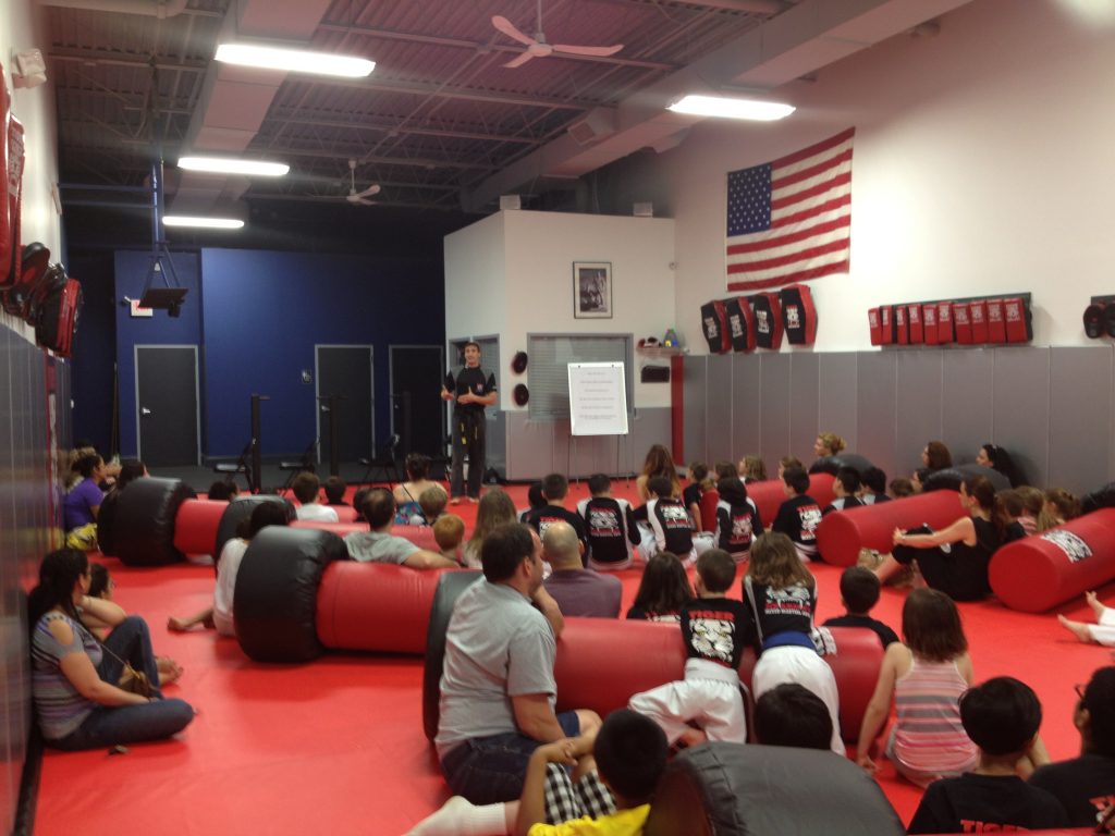 Adults and children sitting on the gym floor with punching bags at Tiger Schulmann's