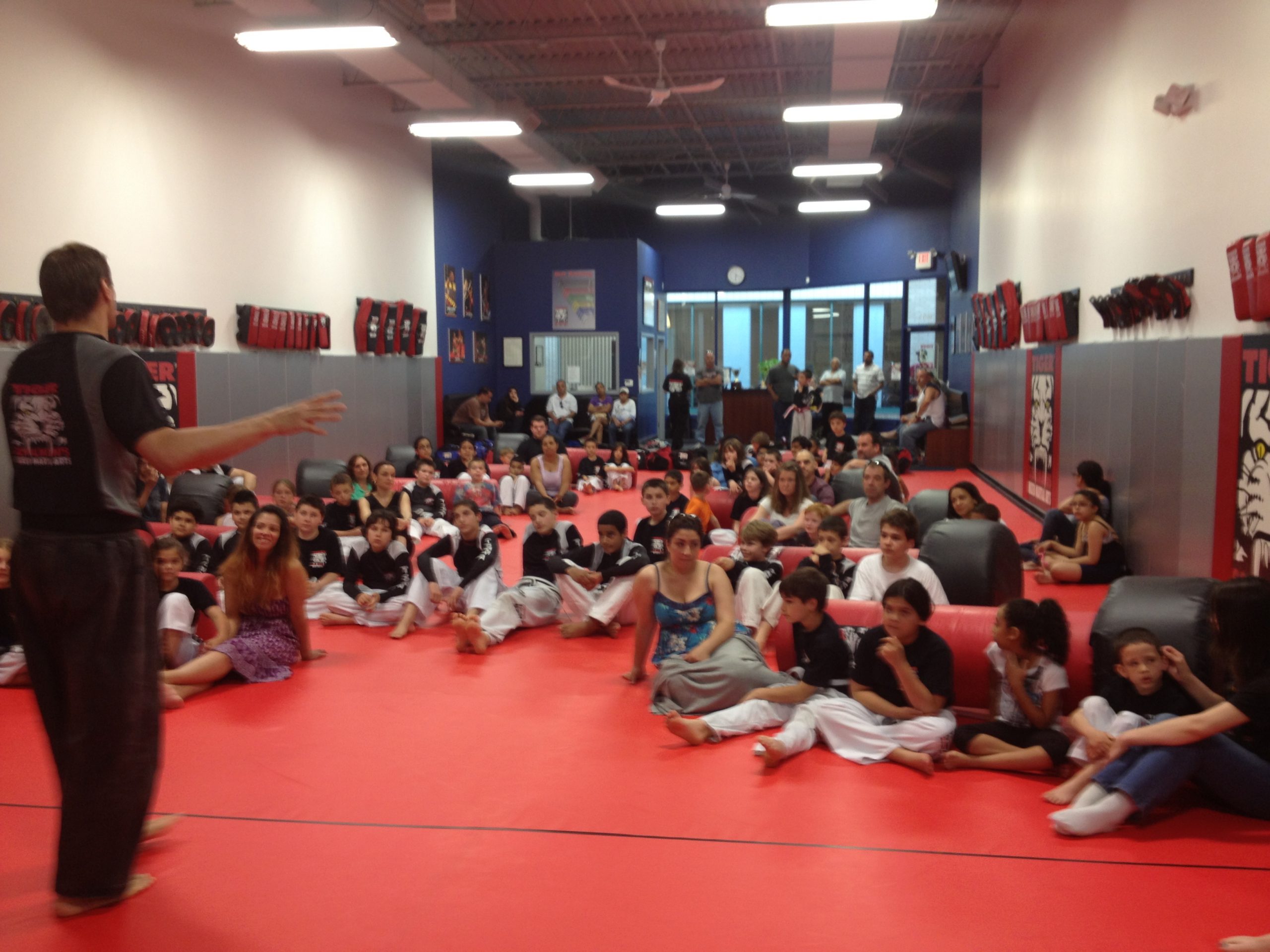 Adults and children sitting on the gym floor with punching bags at Tiger Schulmann's