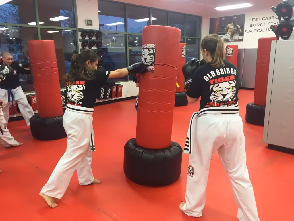 Two women kickboxers punching a bag with other fighters at Tiger Schulmann's gym