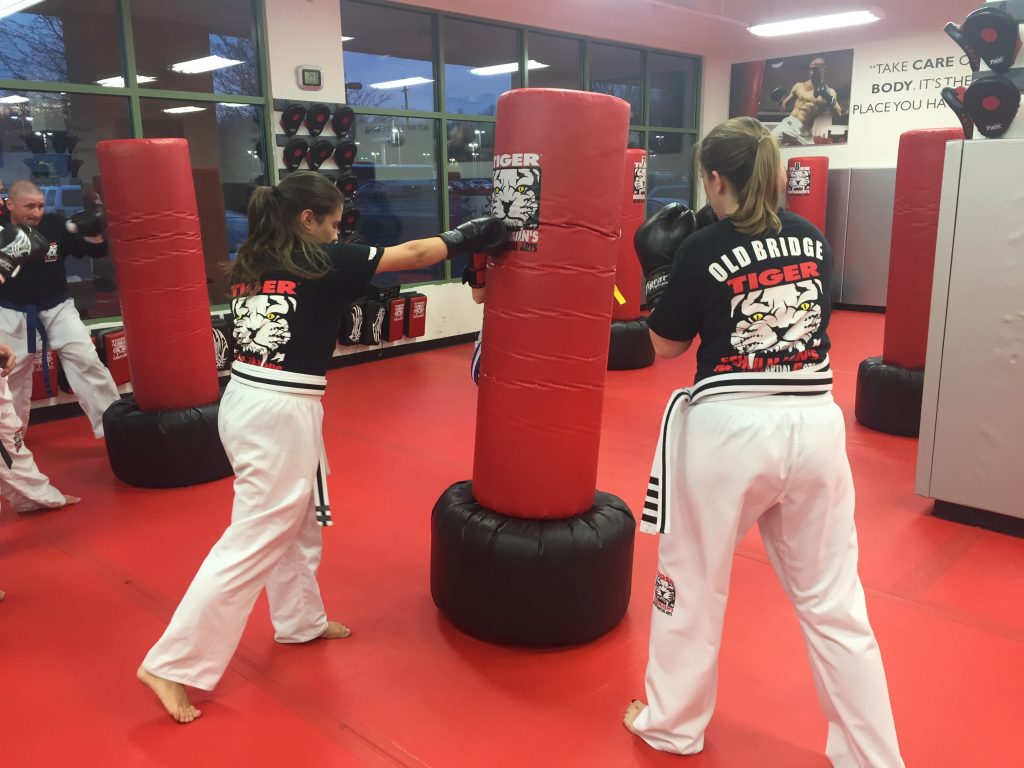Two women kickboxers punching a bag with other fighters at Tiger Schulmann's gym