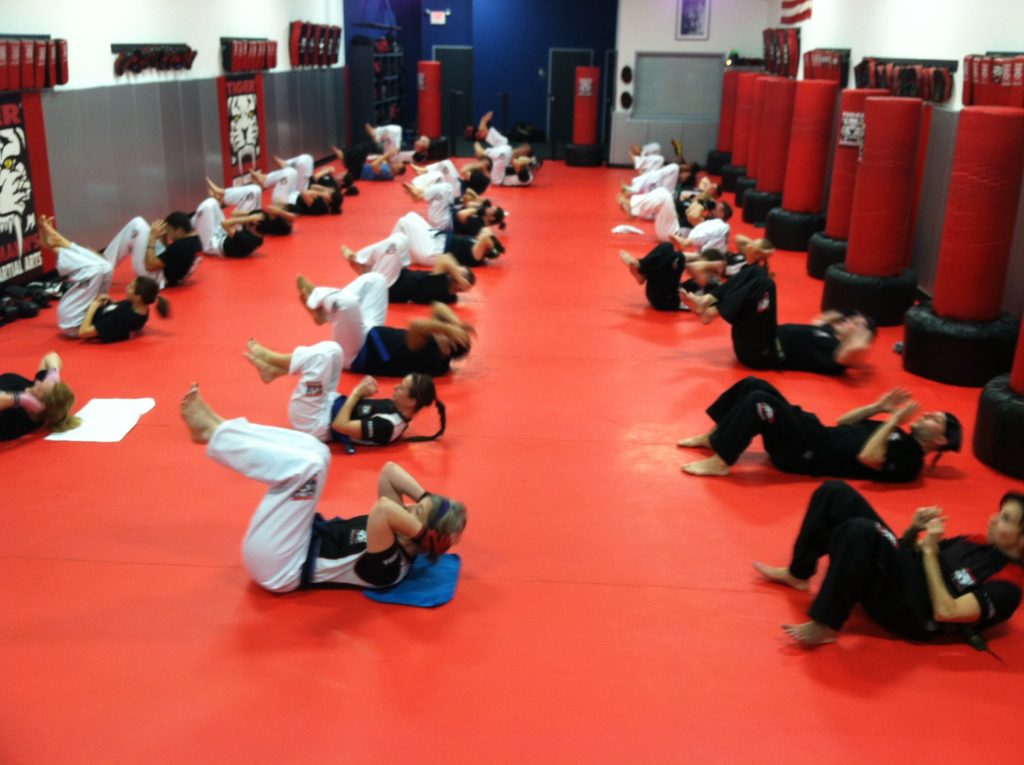 Adult kickboxers doing sit ups on the red gym floor at Tiger Schulmann's