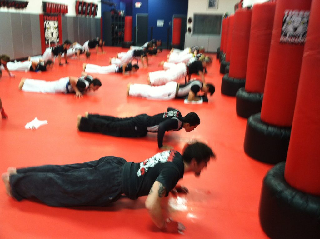 Adult kickboxers doing push ups on the red gym floor at Tiger Schulmann's