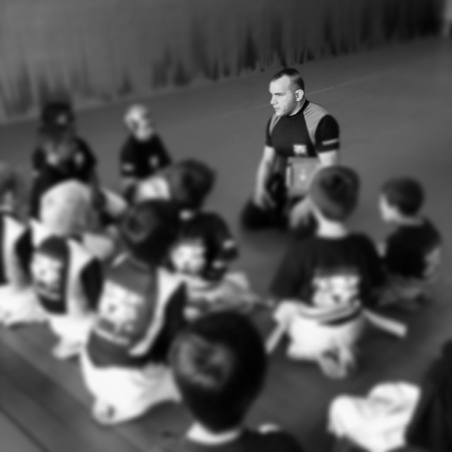 Martial arts instructor lecturing the children sitting on a gym floor at Tiger Schulmann's