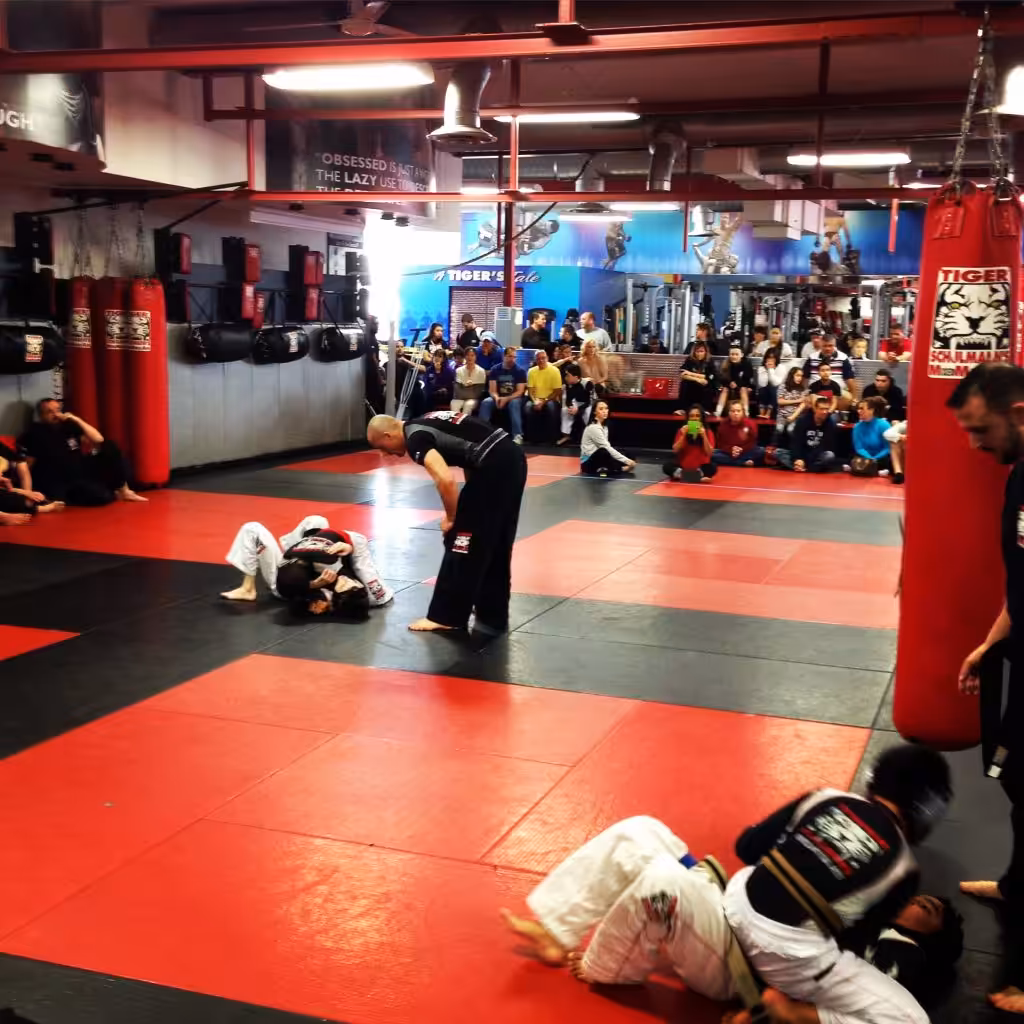 Two boys fighting on the gym floor with referee above and parents watching at Tiger Schulmann's