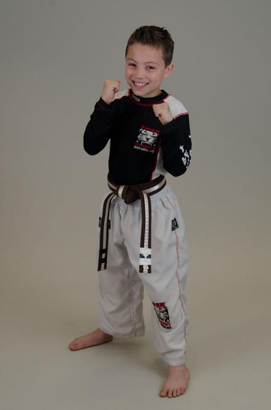 A Boy Standing with fists up smiling in Tiger Schulmann's gear