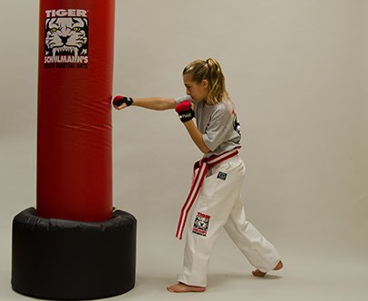 A Girl in Tiger Schulmann's gear Punching a red punching bag