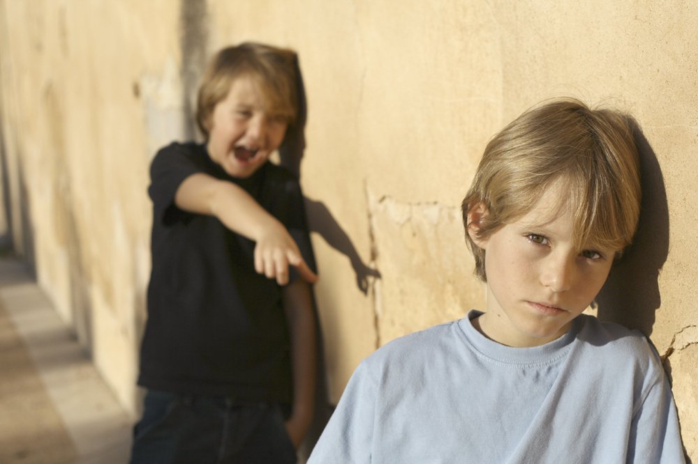 A boy in black shirt bullies a boy in pale blue shirt