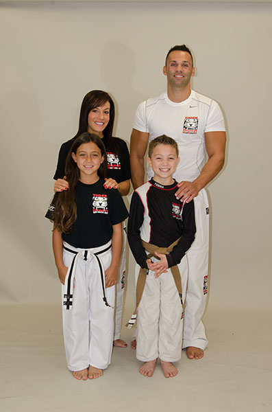 A man and woman with a boy and a girl in Tiger Schulmann's gear posing and smiling