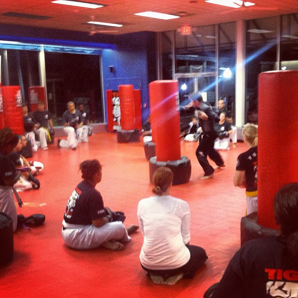 Kickboxing class for adults with punching bags and instructor monitoring the training