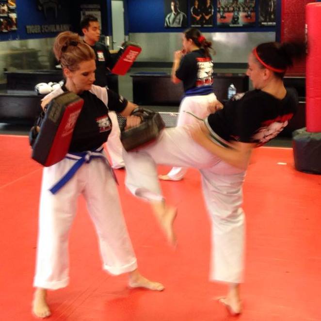 Woman kickboxer practicing kicking with other fighters at Tiger Schulmann's gym