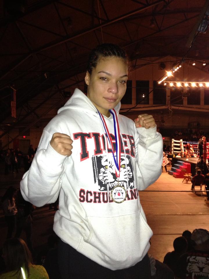 A woman kickboxer with a medal around her nech and clinched fists