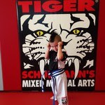 Blue Belter Boy Posing with fists up at Tiger Schulmann's with a tiger logo behind