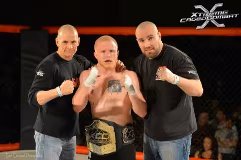 MMA fighter Craig Alexander with the championsip belt in the ring with his two coaches
