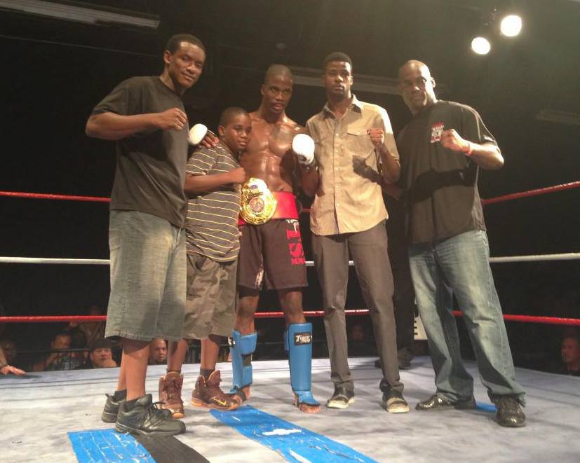 MMA fighter with a championship belt and his Tiger Schulmann's team in the ring