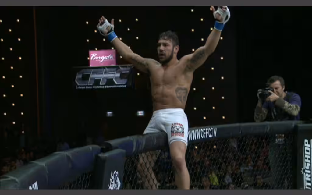 Tiger Schulmann's fighter sitting on the edge of the octagon with his hands raised