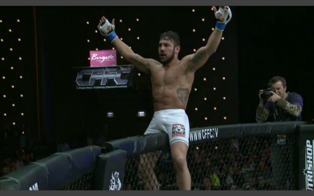 Tiger Schulmann's fighter sitting on the edge of the octagon with his hands raised