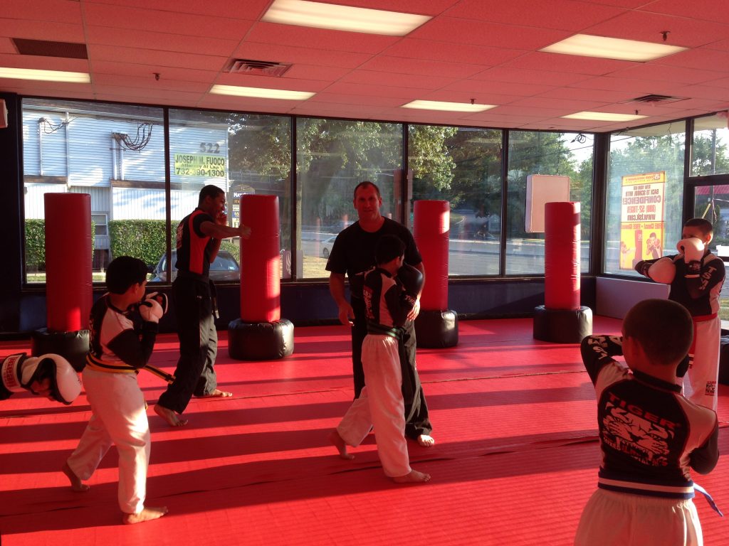 Four boys practicing punching with two instructors at Tiger Schulmann's red gym with big windows