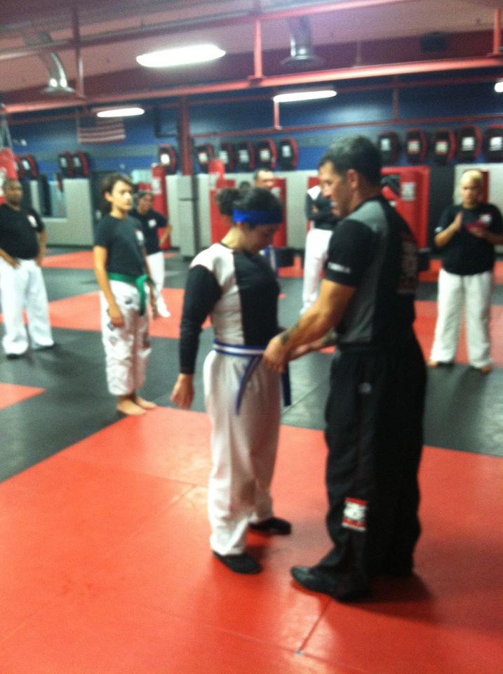 A Woman gets Blue Belt promotion from instructor with others watching