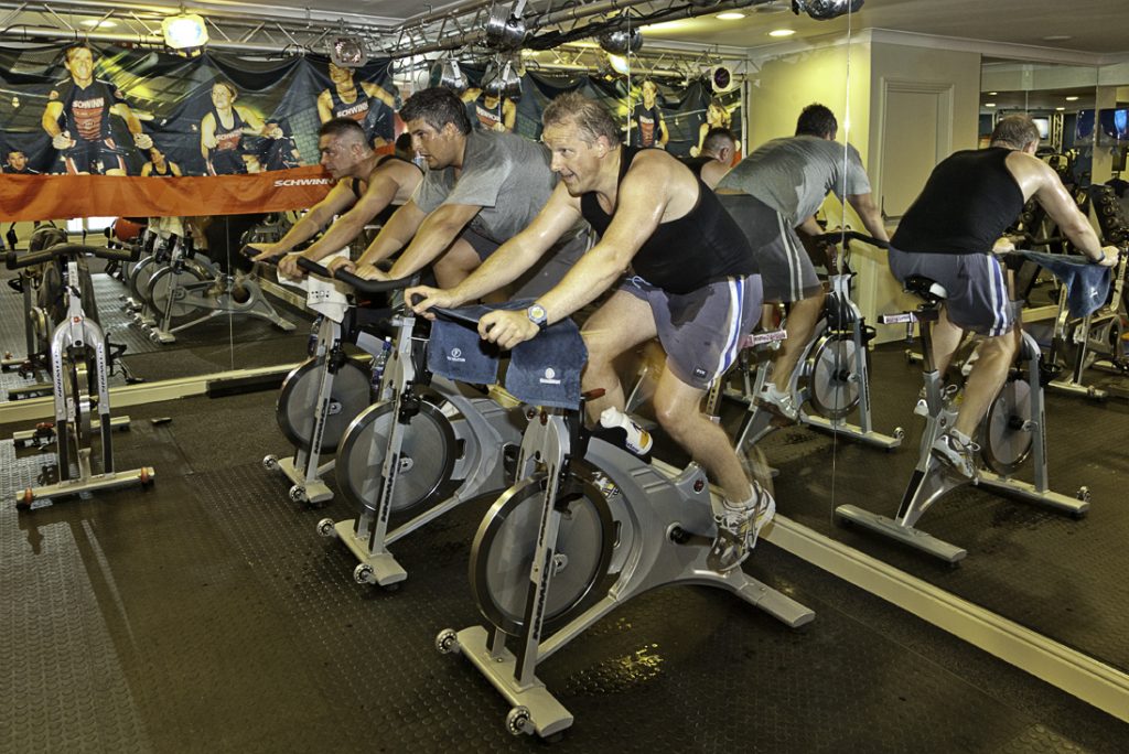 Three Men Using Stationary Bicycle at Tiger Schulmann's with a mirror behind