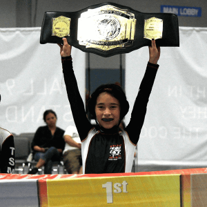 Little girl holds up her winning belt at martial arts tournament