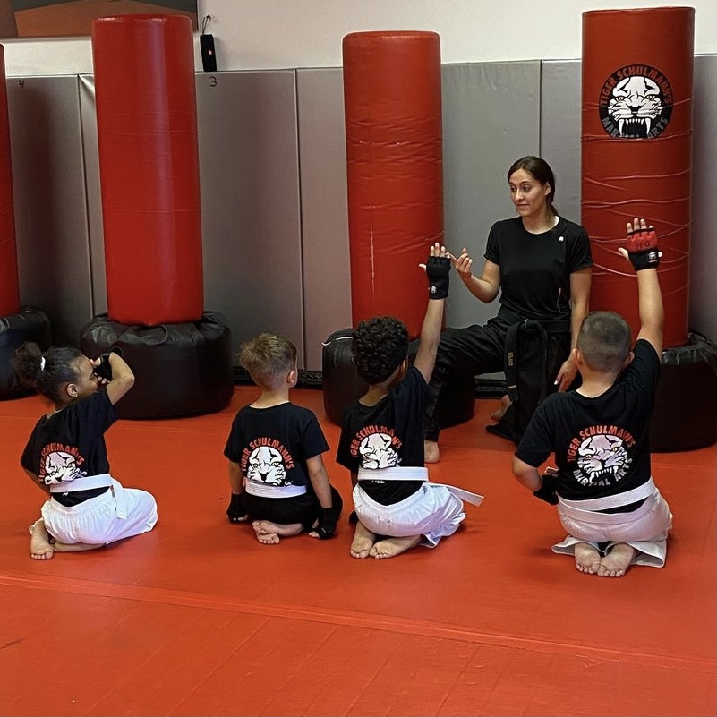 Four kids sitting during a martial arts training with their lady instructor