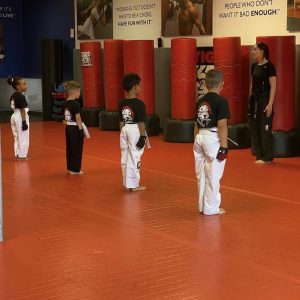 Four kids standing during a martial arts training with their lady instructor