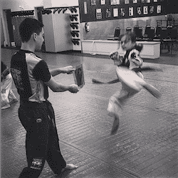 Little girl performing a kick with martial arts instructor