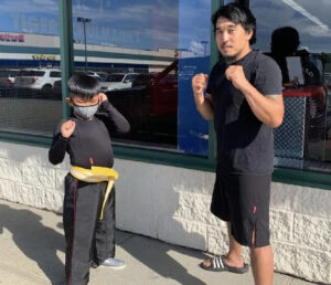 A boy and a man posing in fighting stance outdoors in Garden City