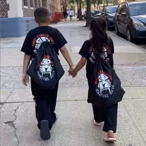 A boy and a girl in Tiger Schulmann's equipment holding hands on the street