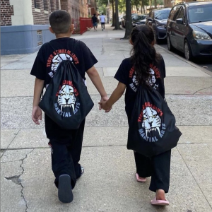 A boy and a girl in Tiger Schulmann's equipment holding hands on the street
