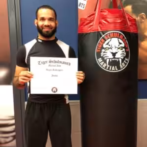 MMA fighter posing with certificate with a punching bag next to him at Tiger Schulmann's