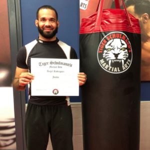 MMA fighter posing with certificate with a punching bag next to him at Tiger Schulmann's
