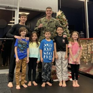 A man in uniform with six children in front of a Christmas tree