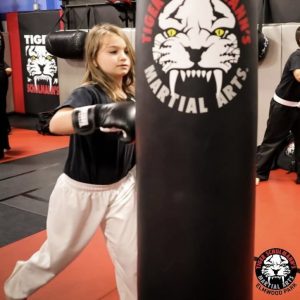 A little girl punching a black punching bag