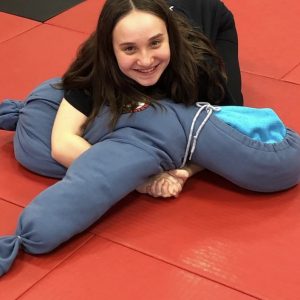 A girl grapples a kickboxing dummy on a red gym floor