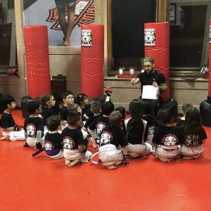 Kids sitting on their knees and listening to their karate instructor