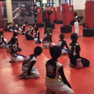 Kids sitting on their knees and watching their karate instructor