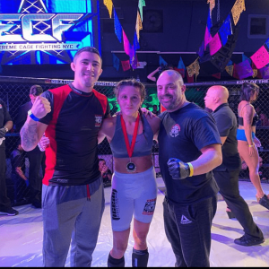 A woman ECF fighter with two members of her crew in the octagon