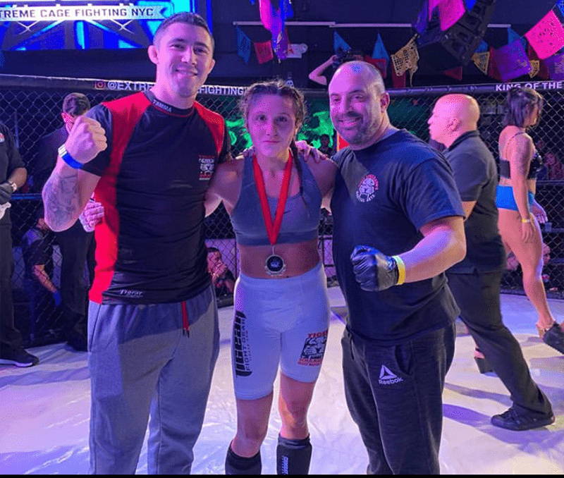 A woman ECF fighter with two members of her crew in the octagon