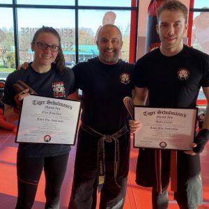 A man and a woman showing Tiger Schulmann's Level one instructor certificates