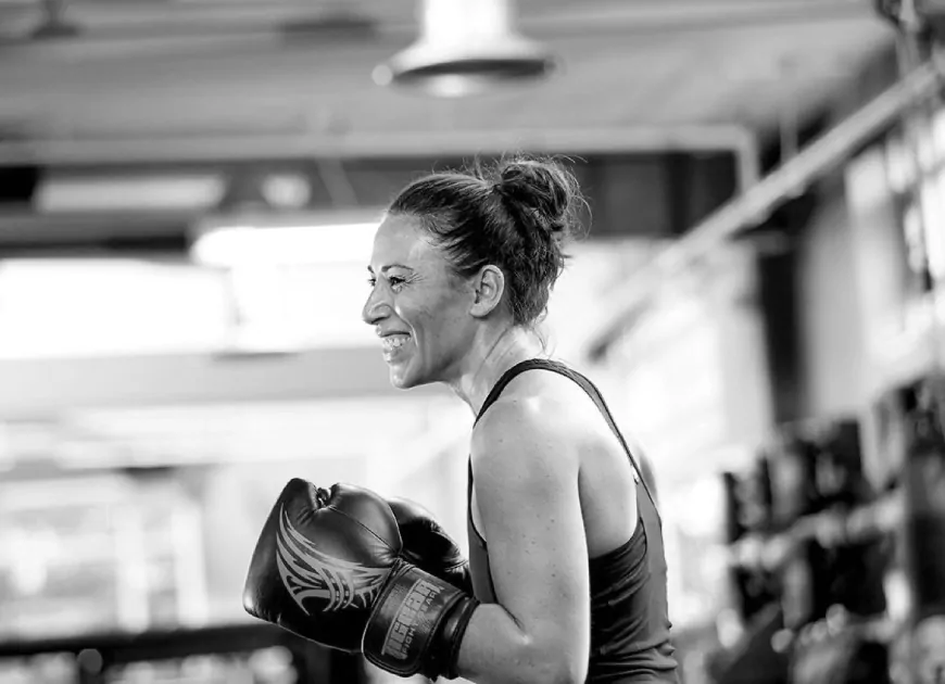 A smiling woman wearing boxing gloves