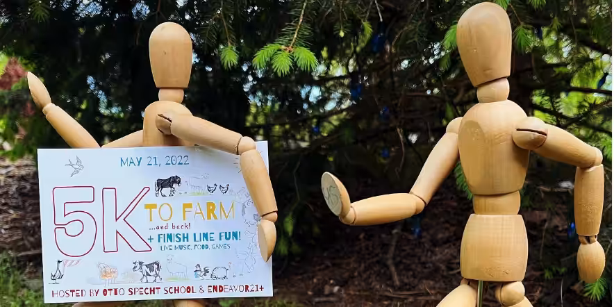 Two wooden figures in nature with 5k sponsored by Tiger Schulmann's sign